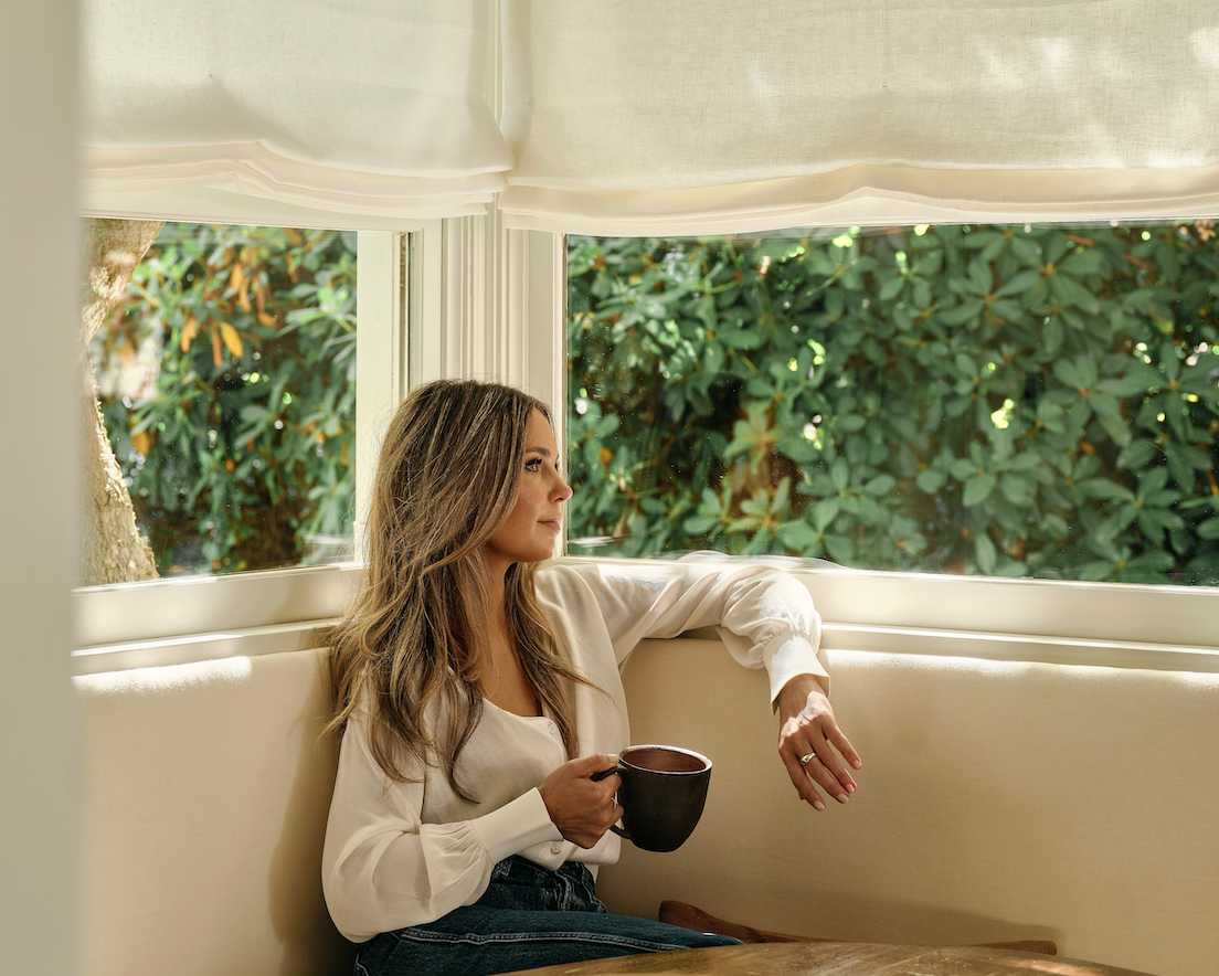 Molly Kidd seated in a breakfast nook beneath soft window treatments.